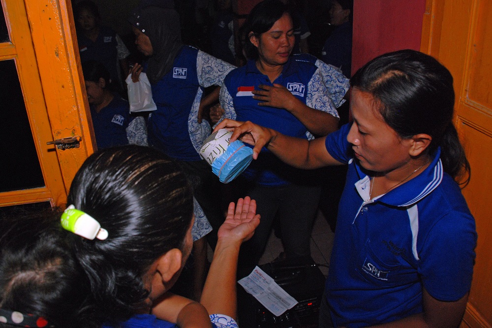 Female union members hold arisan meetings not just to collect a pooled fund, but also to provide an opportunity for political education. (Hari Nugroho) A woman tips a coin tin over another woman's open palm.